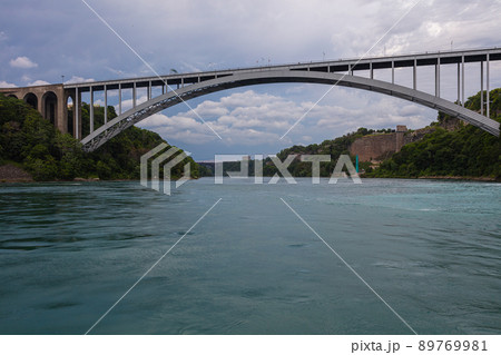 Niagara Falls, Canada - August 27, 2021: The Rainbow Bridge at Niagara Falls is a steel arch bridge that spans the Niagara Gorge. She connects Ontario, Canada and New York, United States. Niagara Falls, Canada - August 27, 2021: The Rainbow Bridge at Niagara Falls is a steel arch bridge that spans the Niagara Gorge. She connects Ontario, Canada and New York, United States. 89769981