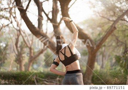 Athletic woman warming up before a workout standing facing the early morning rising sun at park Athletic woman warming up before a workout standing facing the early morning rising sun at park 89771151