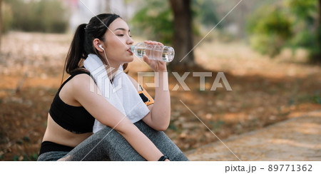 Young woman athlete takes a break, drinking water, out on a run on a hot day. Young woman athlete takes a break, drinking water, out on a run on a hot day. 89771362