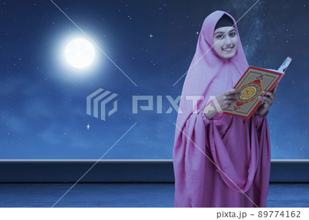 Asian Muslim woman in a veil standing and holding the Quran 89774162