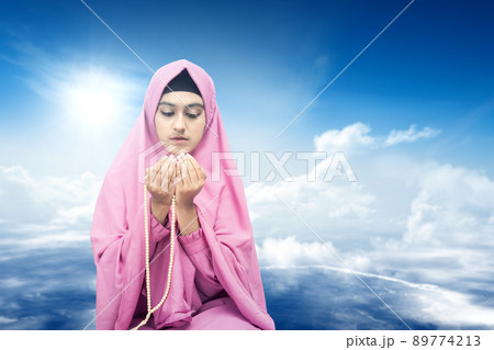 Asian Muslim woman in veil praying with prayer beads on her hands Asian Muslim woman in veil praying with prayer beads on her hands 89774213