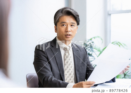 書類を見ながら手前の人物と話をするビジネスマン 89778426