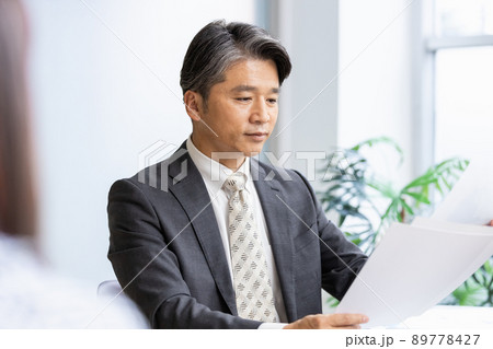 書類を見ながら手前の人物と話をするビジネスマン 89778427
