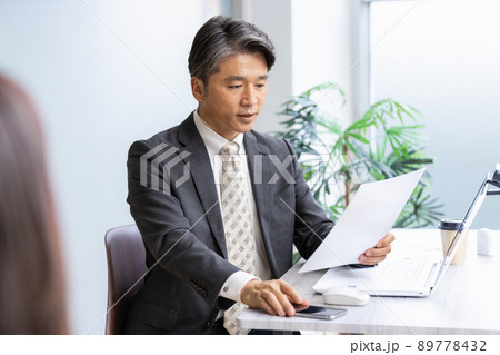 書類を見ながら手前の人物と話をするビジネスマン 89778432