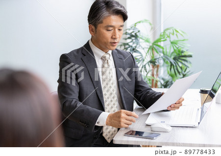 書類を見ながら手前の人物と話をするビジネスマン 書類を見ながら手前の人物と話をするビジネスマン 89778433