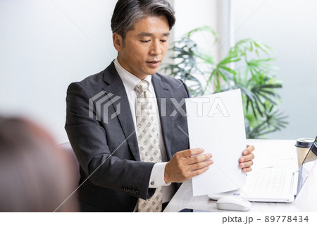 書類を見ながら手前の人物と話をするビジネスマン 89778434