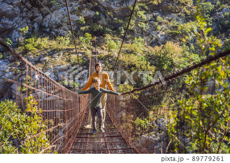 Father and son tourists on Old rusty bridge. Attraction Long extreme suspension iron bridge across the river Moraca. Sights of Montenegro. Landmark Montenegro 89779261