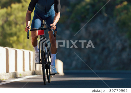 Male cyclist riding racing bicycle, man cycling on countryside summer road. Training for triathlon or cycling competition 89779962