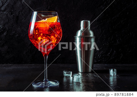 Aperol cocktail with a fresh orange slice and a shaker, a side view on black 89781884