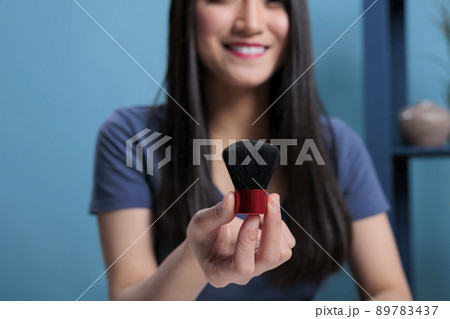 Pov of content creator holding brush reviewing makeup product to her fans while filming beauty videoblog in studio with blue background. Social media influencer recording make up tutorial. Close up 89783437