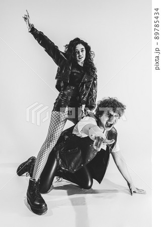 Monochrome portrait of crazy musicians, young couple wearing black leather outfits gesturing, moving on white studio background. Music, youth 89785434