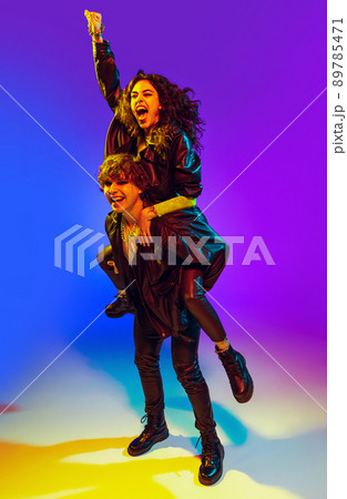 Young couple of rock-and-roll musicians wearing black leather outfits gesturing, shouting and posing on blue yellow background in neon light 89785471
