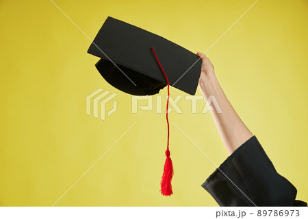 Front view of female hand raising, holding, showing mortarboard. Girl wearing graduate gown graduating from college, university, high school. Isolated on green background. Front view of female hand raising, holding, showing mortarboard. Girl wearing graduate gown graduating from college, university, high school. Isolated on green background. 89786973