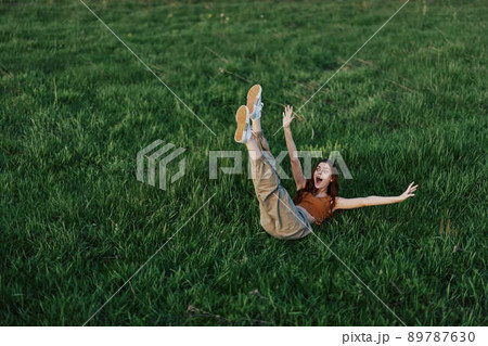 A young woman playing games in the park on the green grass spreading her arms and legs in different directions falling and smiling in the summer sunlight A young woman playing games in the park on the green grass spreading her arms and legs in different directions falling and smiling in the summer sunlight 89787630