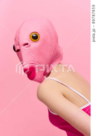 Skinny woman in a pink Halloween costume with a fish head on her face poses funny against a pink background and looks at the camera, art concept photo 89787659