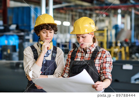 Pensive female engineer looking at sketch on blueprint held by colleague Pensive female engineer looking at sketch on blueprint held by colleague 89788444