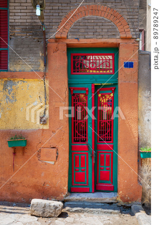 Old grunge decorated door painted in green and red vibrant colors on orange painted stone wall Old grunge decorated door painted in green and red vibrant colors on orange painted stone wall 89789247
