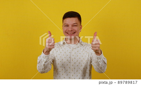 Happy smiling guy 20 years old in a white shirt shows thumbs up on a yellow background. OK Happy smiling guy 20 years old in a white shirt shows thumbs up on a yellow background. OK 89789817