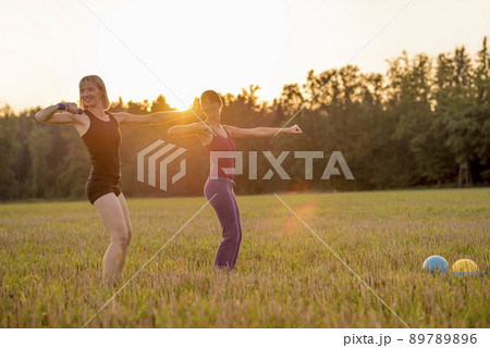 Two fit young women working out with dumbbells standing in the middle of beautiful autumn grassland 89789896