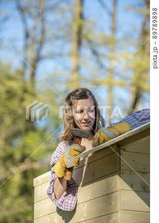DIY concept - young woman holding a hammer working on a wooden playhouse 89789898