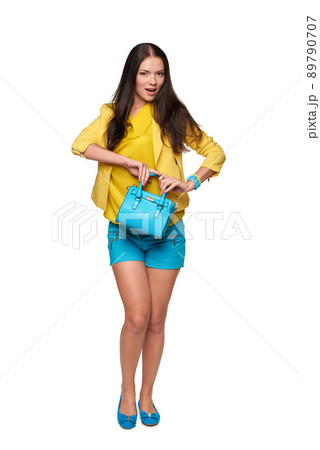 Playful young girl in yellow and blue clothes with blue hand bag standing looking at camera 89790707