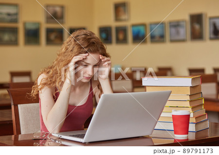 Task, test, learning and education concept. Intelligent, reader girl wearing casually sitting at desk in reading room in front of laptop, keeps hands on forehead, preparing for important exam. Task, test, learning and education concept. Intelligent, reader girl wearing casually sitting at desk in reading room in front of laptop, keeps hands on forehead, preparing for important exam. 89791173
