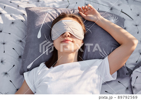 Outdoor shot of young brunette female wearing white casual style t shirt and sleeping mask lying on bed and sleeping, enjoying fresh air and sunshine. Outdoor shot of young brunette female wearing white casual style t shirt and sleeping mask lying on bed and sleeping, enjoying fresh air and sunshine. 89792569