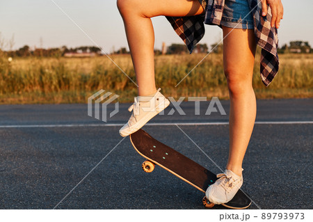 Unknown female person with long beautiful legs wearing white sneakers riding skateboard, faceless skater skateboarding in summertime, outdoor shot. Unknown female person with long beautiful legs wearing white sneakers riding skateboard, faceless skater skateboarding in summertime, outdoor shot. 89793973