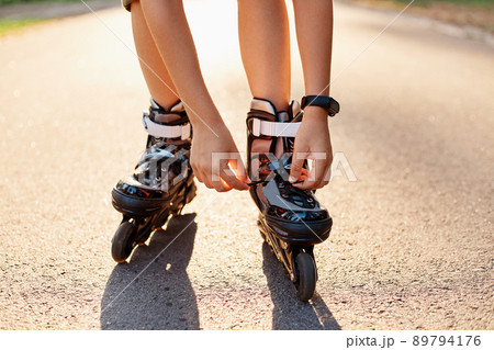 Close-up of an anonymous kid's hands fixing laces on roller blades before skating, unknown child on road in sunny summer day, rollerblading, active lifestyle. 89794176
