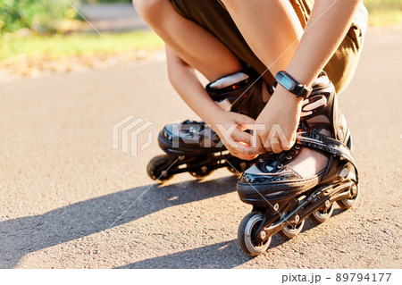 Close up portrait of unknown child squats on road and fixing laces on roller blades before skating, faceless kid having fun outdoor, rollerblading, playing alone. Close up portrait of unknown child squats on road and fixing laces on roller blades before skating, faceless kid having fun outdoor, rollerblading, playing alone. 89794177