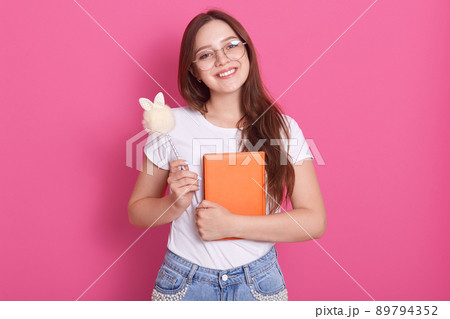 Close up portrait of young attractive woman holding her notebook isolated over rosy background, looks smiling directly at camera, standingwith her textbook organizer and pen in hand. Studying concet. Close up portrait of young attractive woman holding her notebook isolated over rosy background, looks smiling directly at camera, standingwith her textbook organizer and pen in hand. Studying concet. 89794352