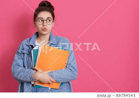 Thoughtful pretty woman looks pensively aside with rounded lips, holds paper folder, has pleasant appearance, being deep in thoughts. Copy space for advertisement. 89794543
