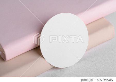 Round white gift tag mockup on beige and pink book background. Blank paper circular price sticker tag mockup 89794585