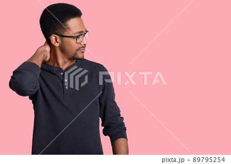 Sideways shot of serious Afro American male manager scratches neck, concentrated aside, wears optical glasses and casual sweater, isolated over pink background with copy space for your promotion Sideways shot of serious Afro American male manager scratches neck, concentrated aside, wears optical glasses and casual sweater, isolated over pink background with copy space for your promotion 89795254