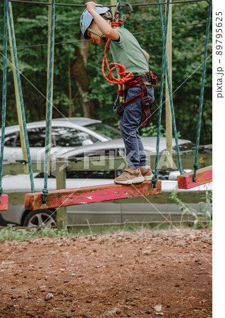 Brave little boy having fun at adventure park and smiling to camera wearing helmet. Scout practicing rappelling. Child - a boy and a girl in the rope park pass obstacles. Brave little boy having fun at adventure park and smiling to camera wearing helmet. Scout practicing rappelling. Child - a boy and a girl in the rope park pass obstacles. 89795625