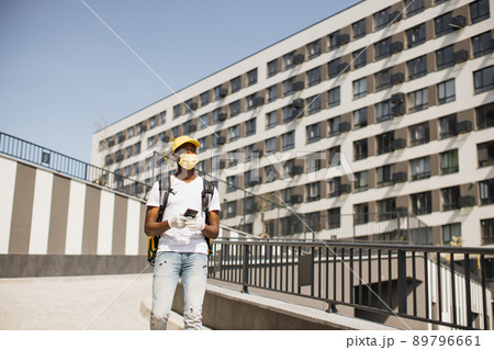 Young African courier in face mask walks down city street with thermal backpack Young African courier in face mask walks down city street with thermal backpack 89796661