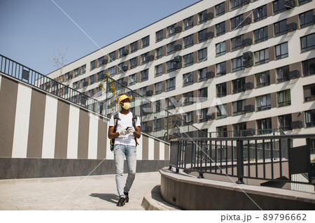 Young African courier in face mask walks down city street with thermal backpack 89796662