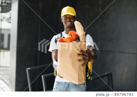 African American courier standing with a package with fresh food from the store. African American courier standing with a package with fresh food from the store. 89796793