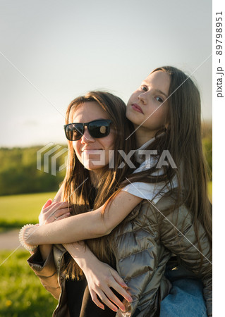 Playful mother giving daughter piggy back ride at green field. Playful mother giving daughter piggy back ride at green field. 89798951