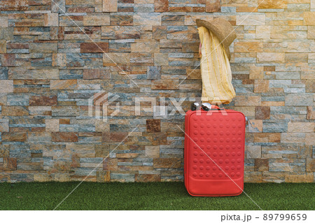 luggage in front of a stone wall and grass floor to use text. suitcase with hat, sunglasses and scarf. graphic resource. 89799659