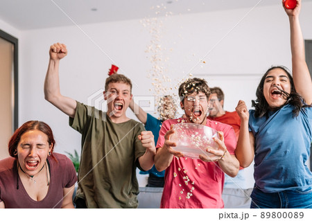 Excited youngsters throwing popcorn in the air after their team's e-sports victory, broadcast on television. 89800089