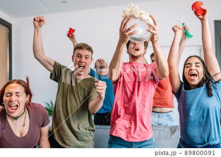 friends jumping for joy, throwing popcorn in the air after their team's victory. group of youngsters partying at home. friends jumping for joy, throwing popcorn in the air after their team's victory. group of youngsters partying at home. 89800091