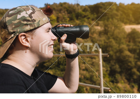 young hiker girl, observing the view from the top of the mountain with her binoculars. concept of hobby and travel. 89800110