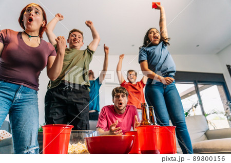 friends jumping for joy watching e-sports on TV after their team's victory. group of young watching soccer on tv. 89800156