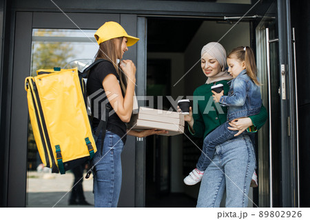 Arabic woman holding her daughter in arms, opens doors of her house and meets delivery woman Arabic woman holding her daughter in arms, opens doors of her house and meets delivery woman 89802926