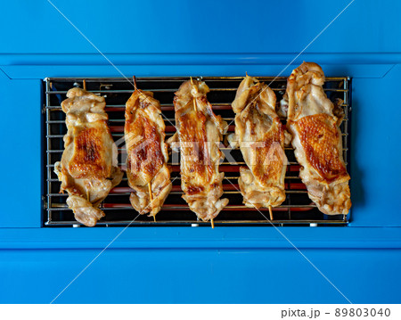 Grilled Chicken stick on the plain blue electric stove from the top view for simple and minimal food background 89803040