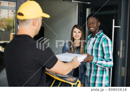 Delivery man in yellow uniform delivering parcel box to recipient - young woman and her husband 89803618