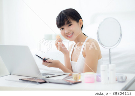 Beauty of young asian woman with learning makeup with powder puff on cheek watching laptop. 89804112