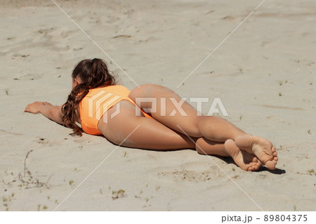 Fit woman in swimsuit sunbathing on sandy beach Fit woman in swimsuit sunbathing on sandy beach 89804375