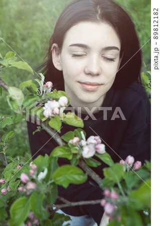 Pretty  teen girl are posing in garden near blossom apple tree with pink flowers. 89812182